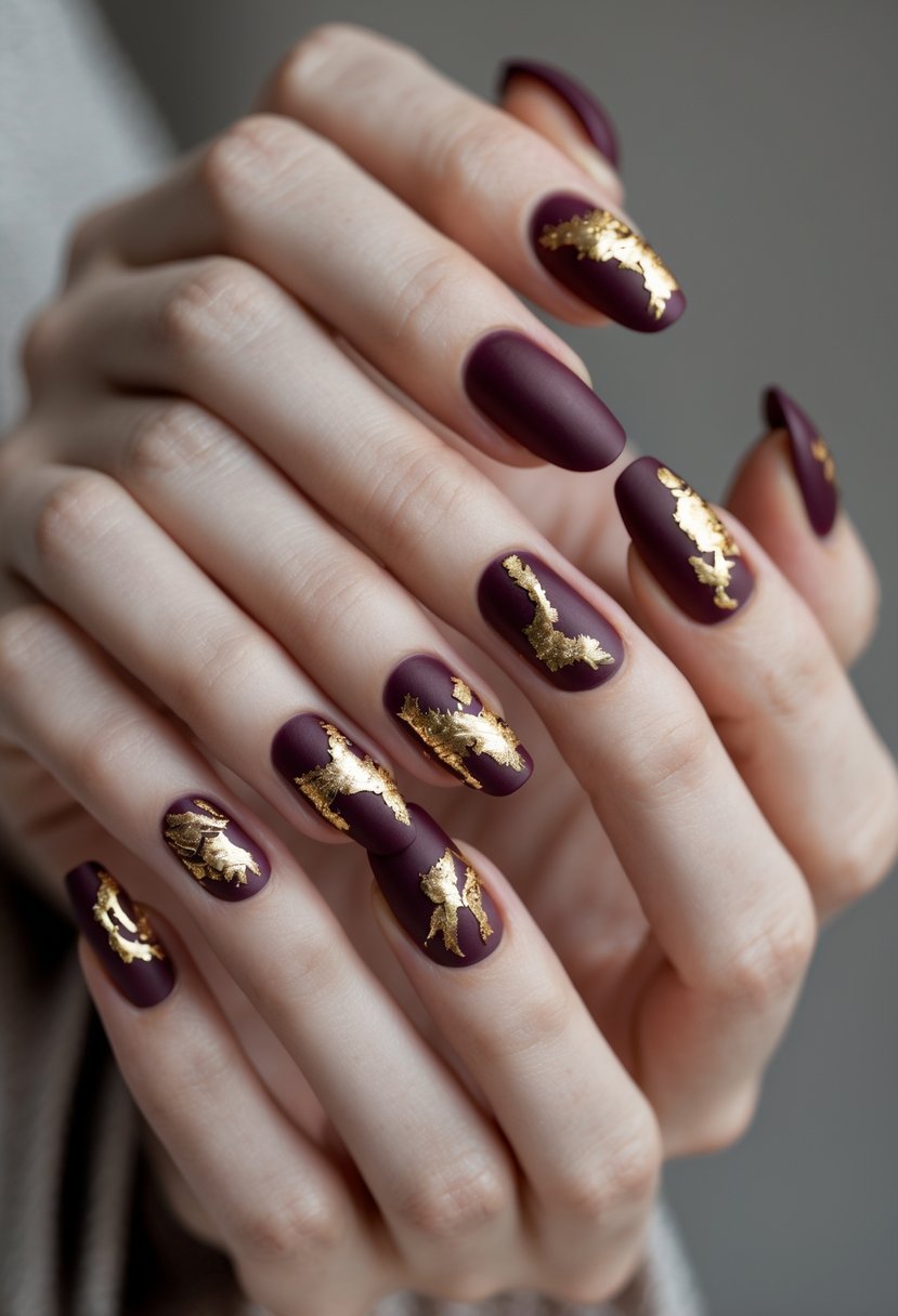 Close-up of a woman's hands showing eight burgundy nails with gold foil accents.