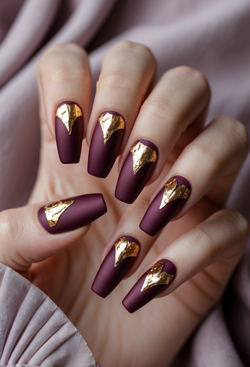 Close-up of a woman's hand with seven burgundy nails featuring gold foil accents.