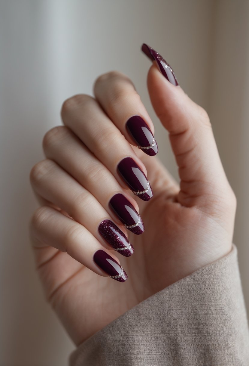 Close-up of a woman's hand with deep burgundy French tip nails featuring glitter accents, posed against a neutral background.