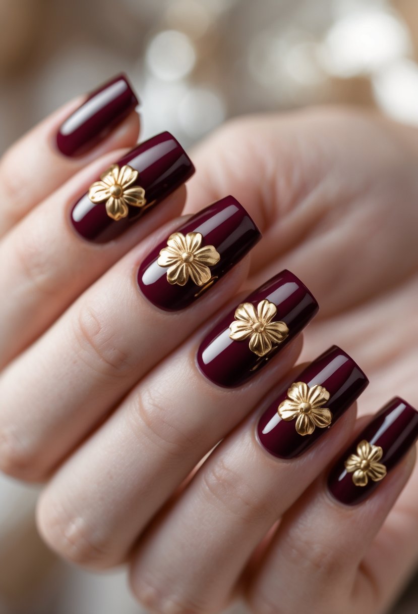 Close-up of a hand with five square burgundy nails decorated with gold flower accents.