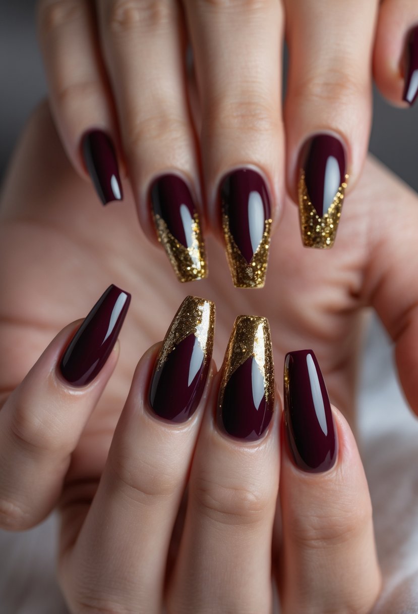 A close-up of a hand with six burgundy coffin-shaped nails decorated with gold glitter accents.